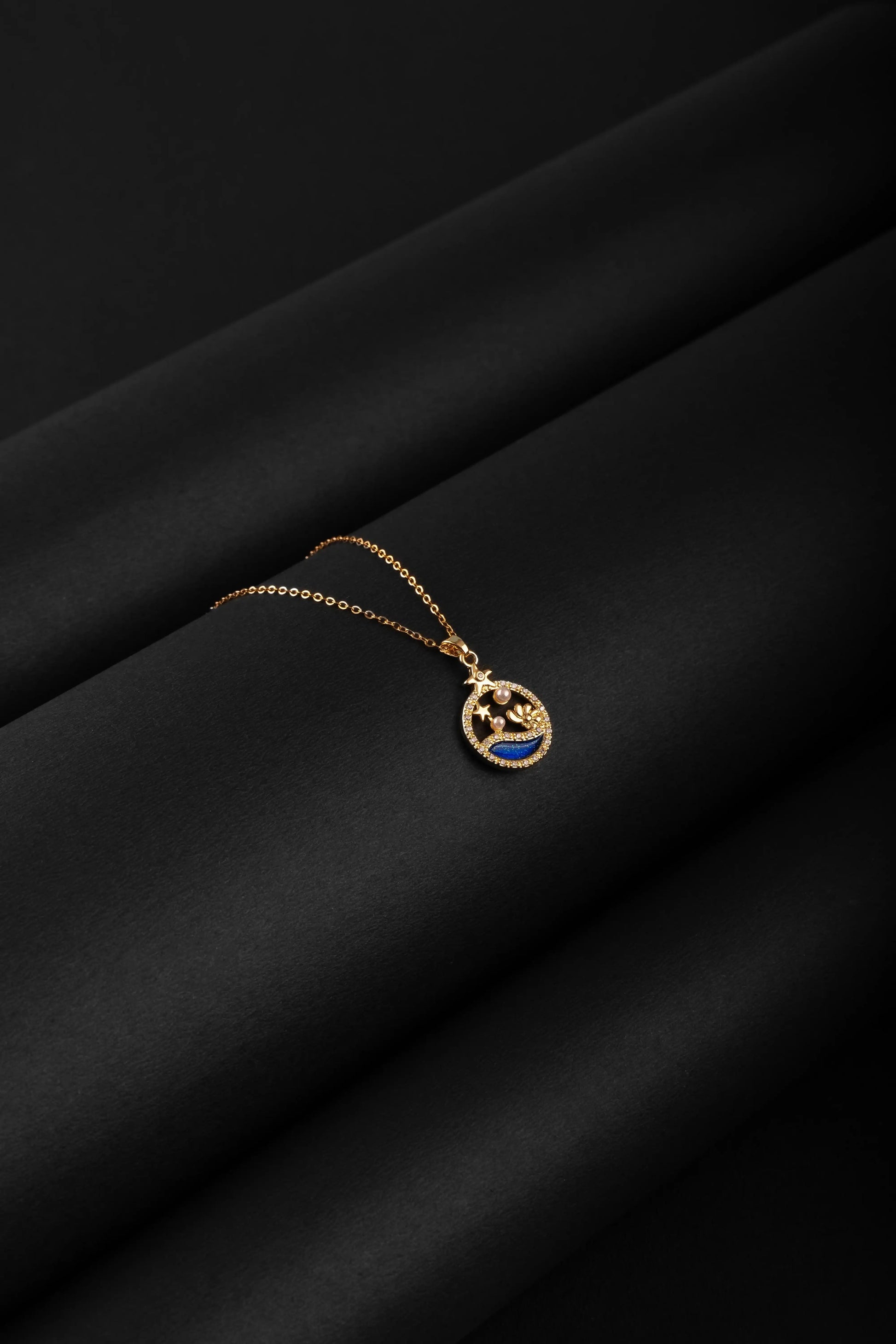 Gold necklace with a blue pendant on a black fabric background