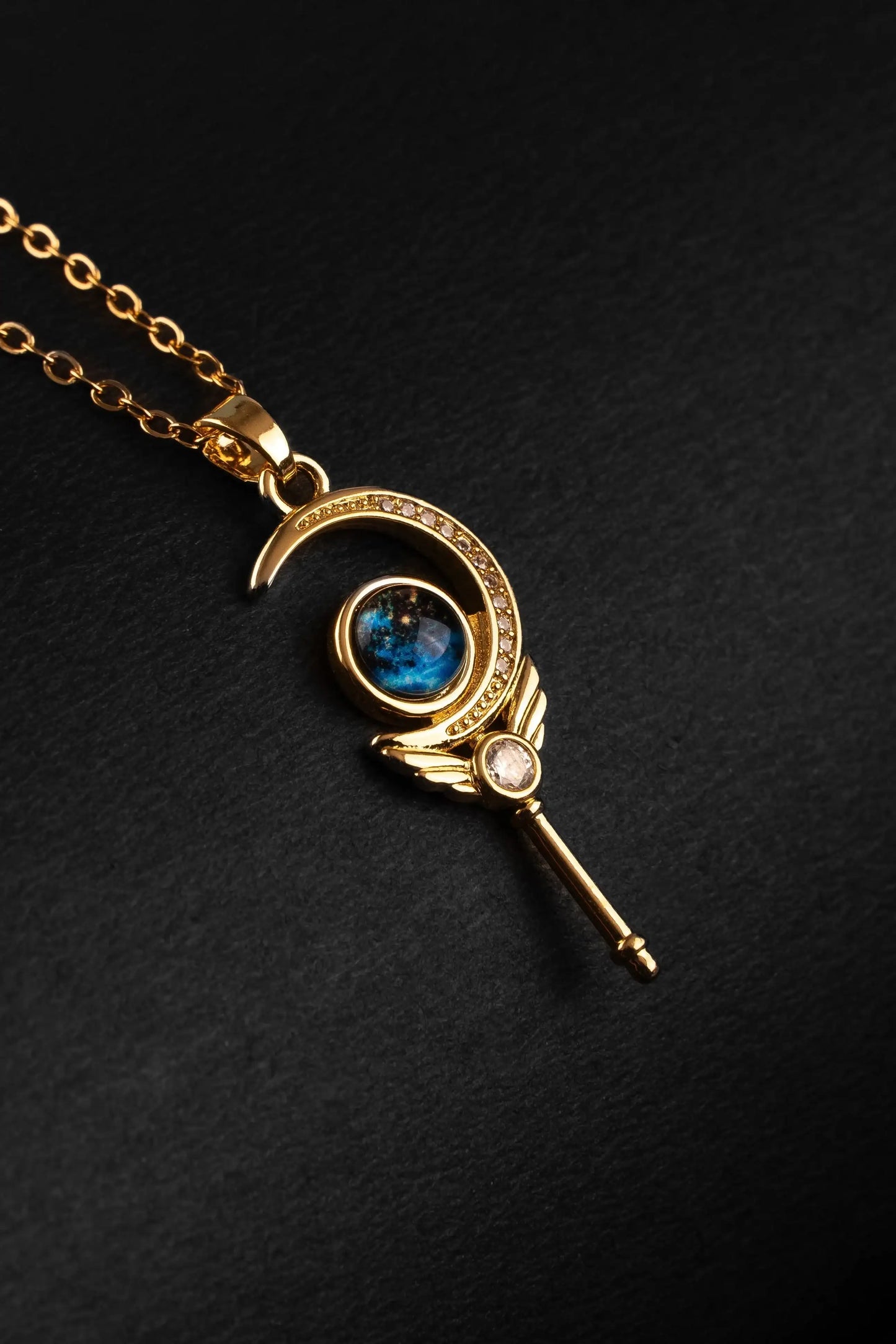 Gold necklace with a moon and key pendant on a black background