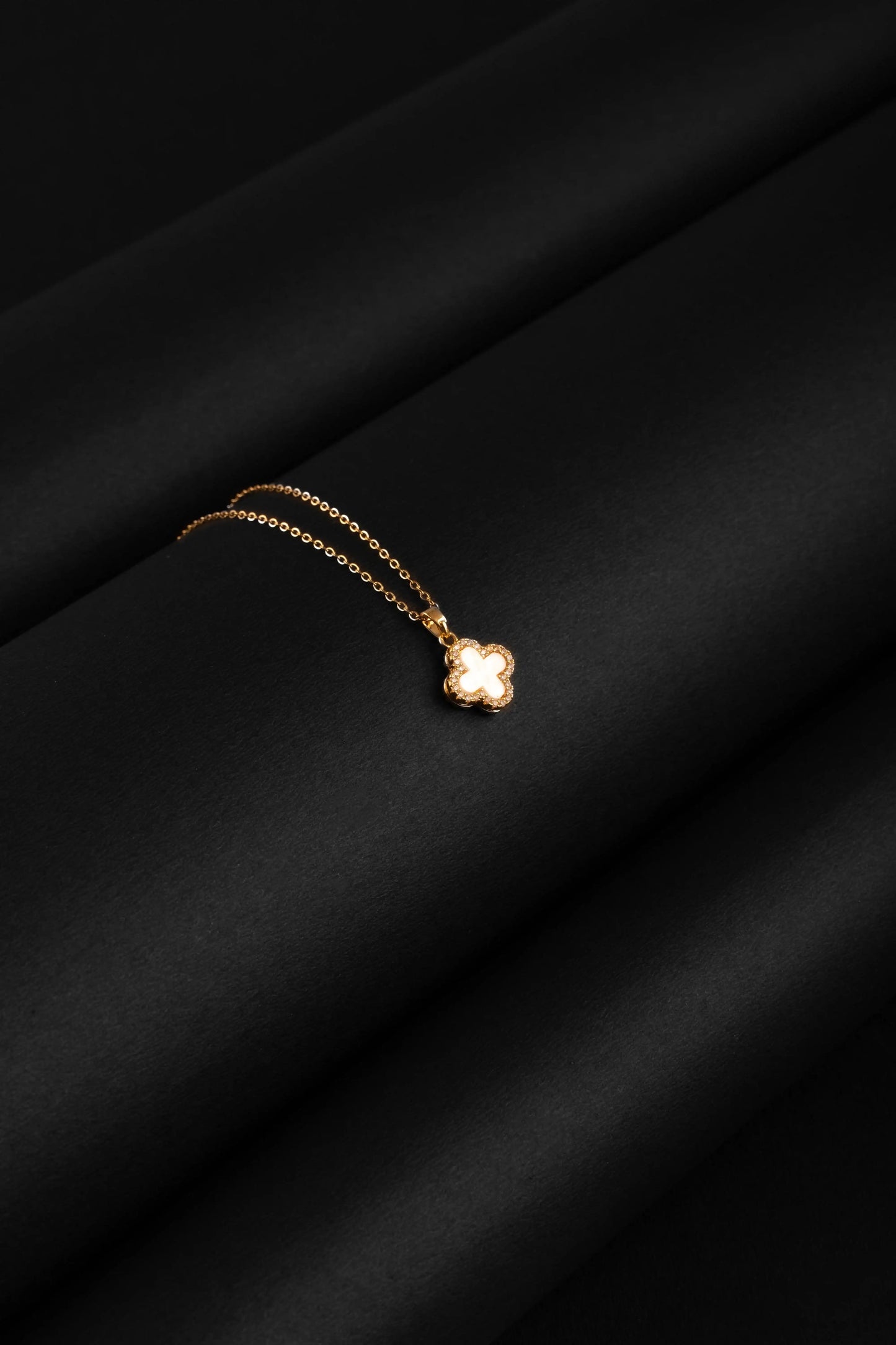 Gold necklace with a clover pendant on a black fabric background