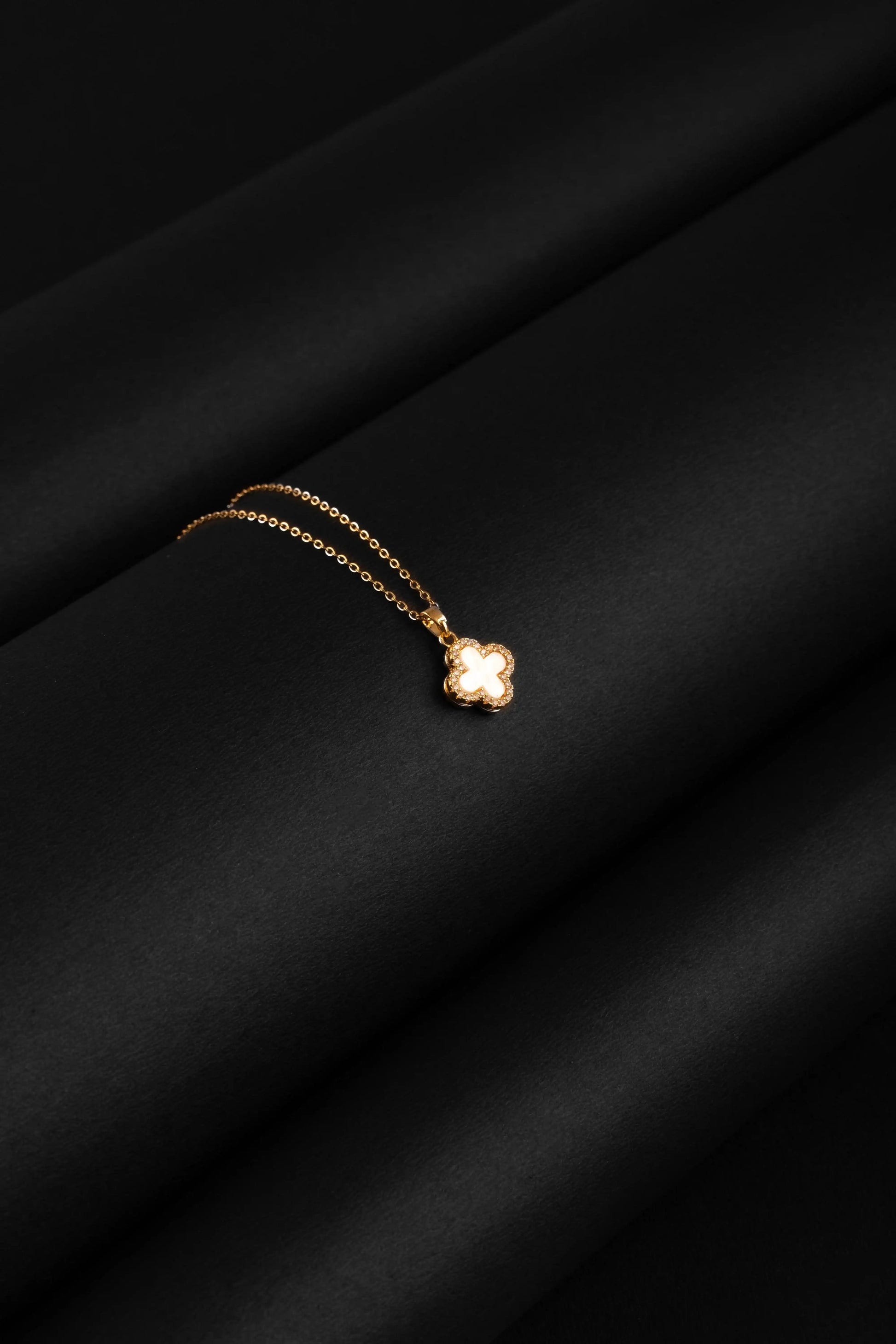 Gold necklace with a clover pendant on a black fabric background