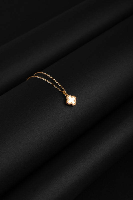 Gold necklace with a clover pendant on a black fabric background