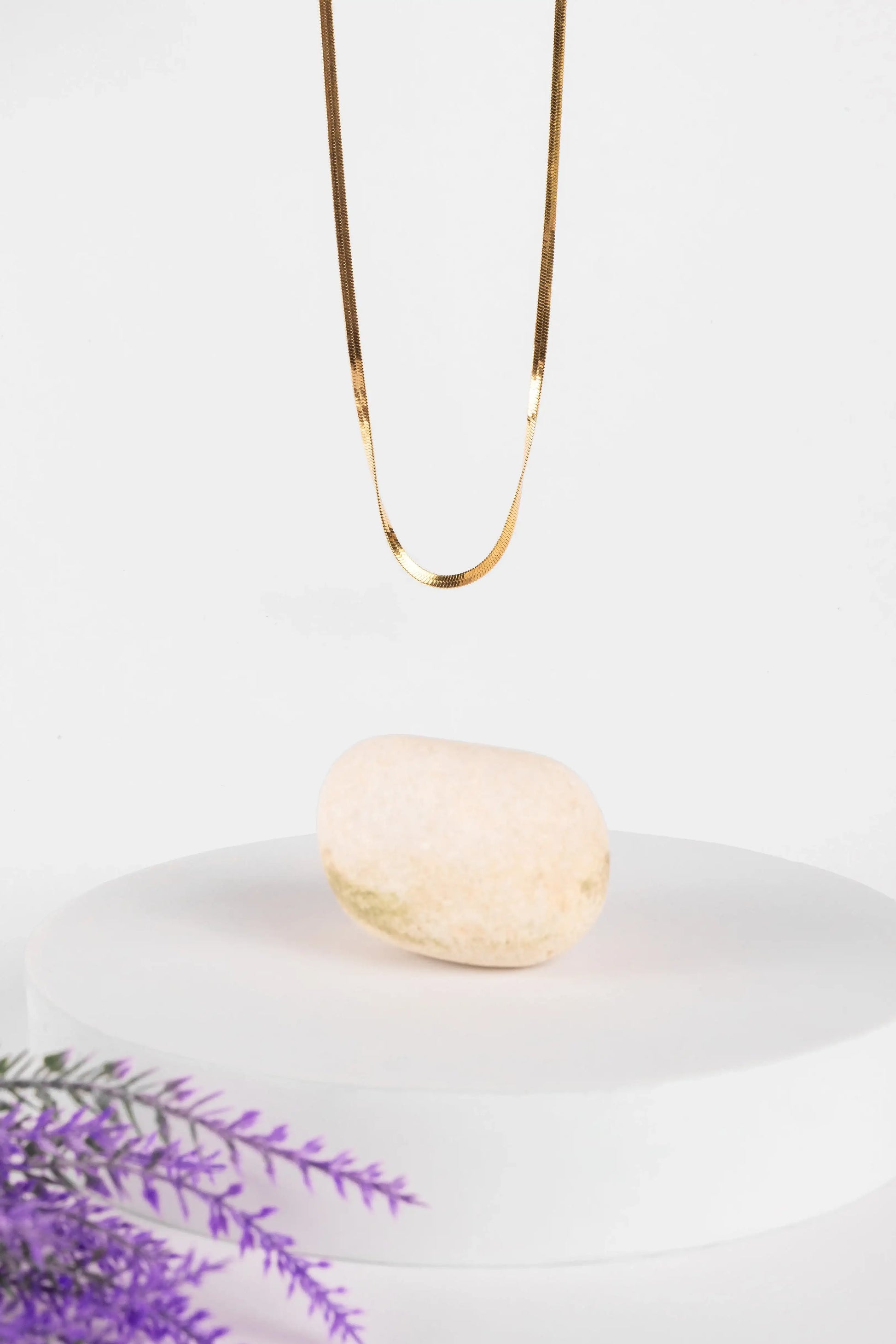 Gold necklace on a white plate with a bar of soap and lavender sprigs.