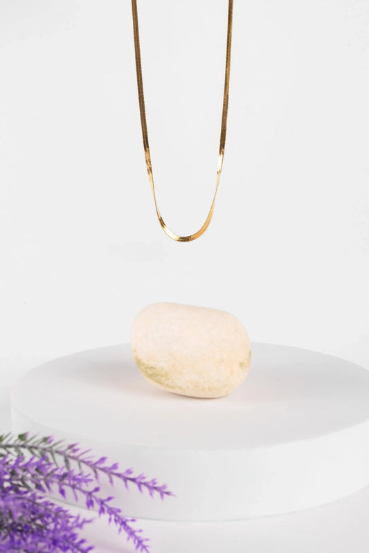 Gold necklace on a white plate with a bar of soap and lavender sprigs.