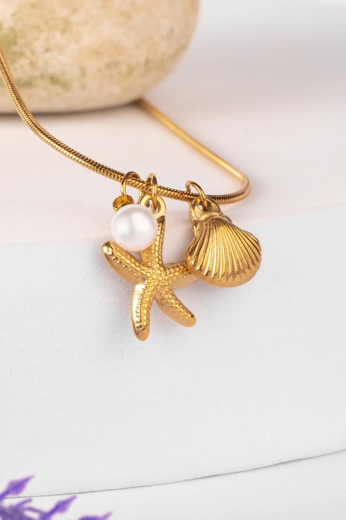 Gold necklace with starfish, shell, and pearl pendant on a white background