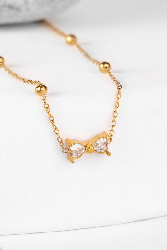 Gold necklace with a bow-shaped pendant on a white background