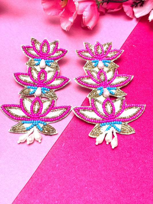 Decorative earrings with pink, gold, and blue design on a pink background