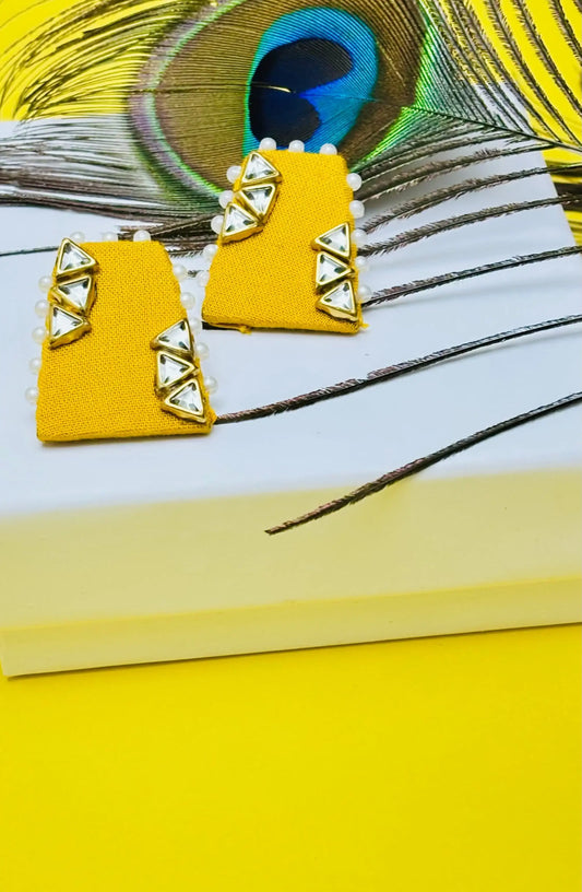 Yellow geometric earrings on a peacock feather and yellow surface