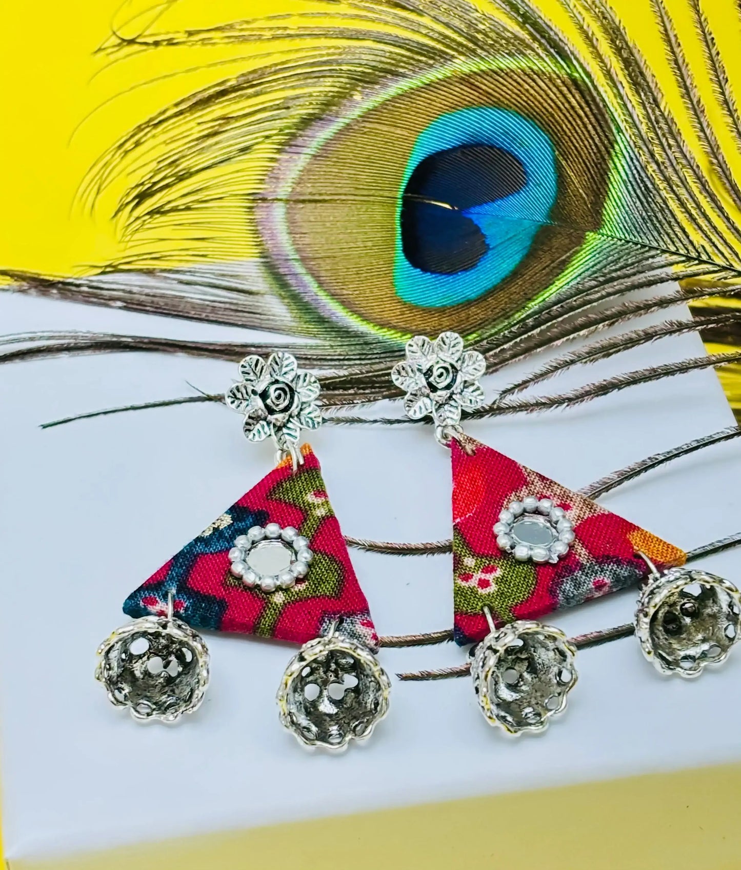 Colorful triangle-shaped earrings with floral patterns on a peacock feather background