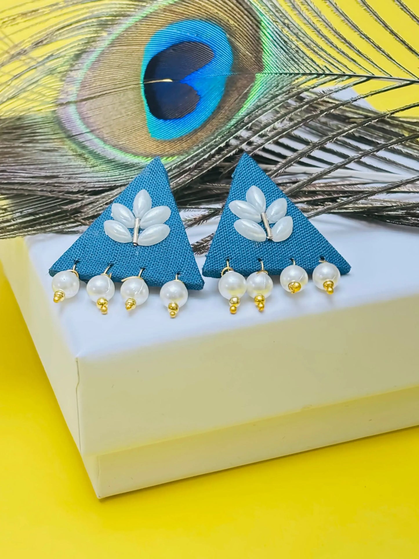Triangular earrings with pearl details on a peacock feather background