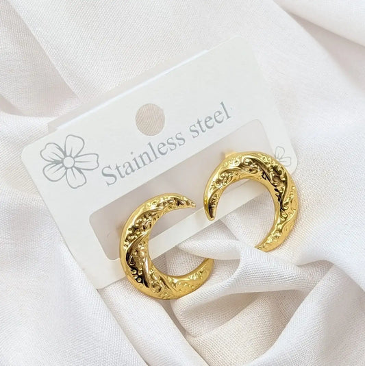 Gold hoop earrings on a white card with 'Stainless steel' text, placed on a white fabric background.