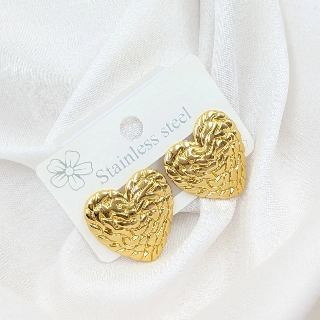 Gold heart-shaped earrings on a white card with 'Stainless steel' text, against a white background.